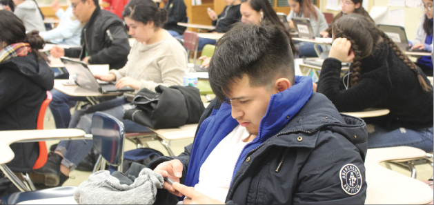 During his third block class,  Junior Uriel Sanchez watches a video on his phone while his classmates complete their work using laptops from the mobile lab. 