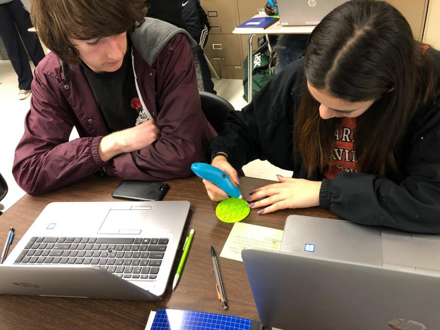 Senior Samuel Throop watches as senior Galilea Pena-Vilagrana uses a 3D pen for the first time during their math analysis class on Feb. 8. Pena Vilagrana chose to trace a series of curved lines as well as the apple logo on her phone. Their teacher, Charles Cuddy, brought in the pens, which were donated by Nebraska Furniture Mart, as well as stencils of various shapes and designs for the class to experiment with. 