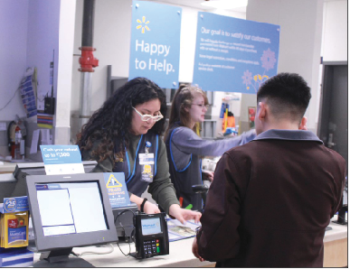 Walmart customer service employee Avigail Morales wears her new vest while helping a customer pay his bill. “It makes me feel glad that I am representing a company that likes to help its environment,” Morales said. “These vests are also more efficient to my job because the pockets are three times bigger.”